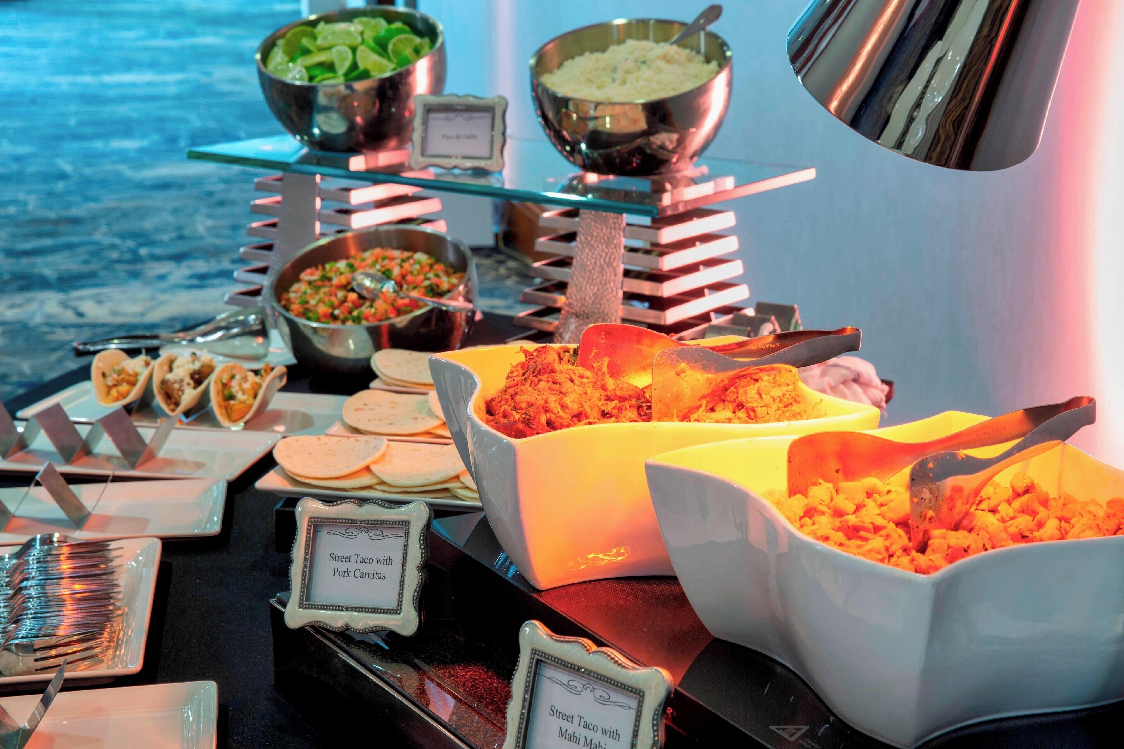 A buffet with various dishes including Street Taco with Pork Carnitas, rice, and a salad.