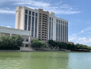 A high-rise hotel with multiple floors, a central courtyard, and a body of water in the foreground.
