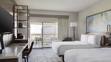 A hotel room with a desk, two beds, a chair, a lamp, and a painting.