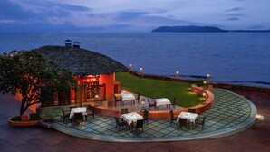 A seaside restaurant with outdoor seating and a thatched-roof structure.