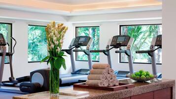 A gym with exercise equipment, a vase with flowers, rolled towels, and a bowl of apples.