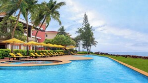 A pool area with yellow sun loungers and umbrellas, surrounded by palm trees and a view of the ocean.