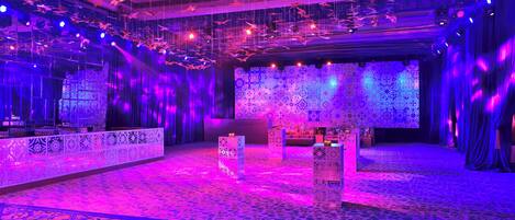 A spacious room with patterned carpet, a stage with a patterned backdrop, and hanging decorations.