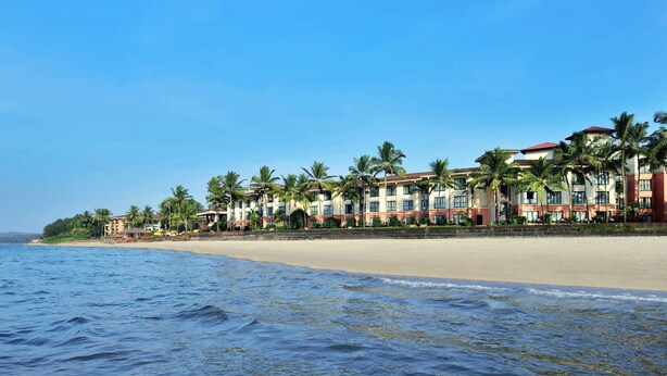 A beachfront hotel with multiple buildings, palm trees, and a sandy beach.