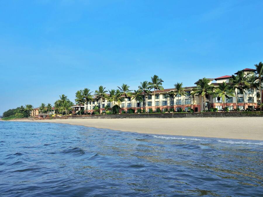 A beachfront hotel with multiple buildings, palm trees, and a sandy beach.