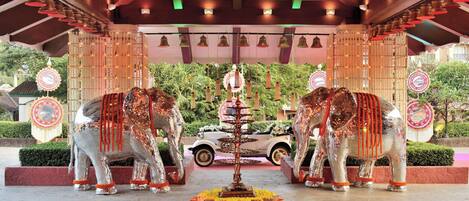 A decorative entrance with two metallic elephant statues, a central fountain, and a white car parked in the background.