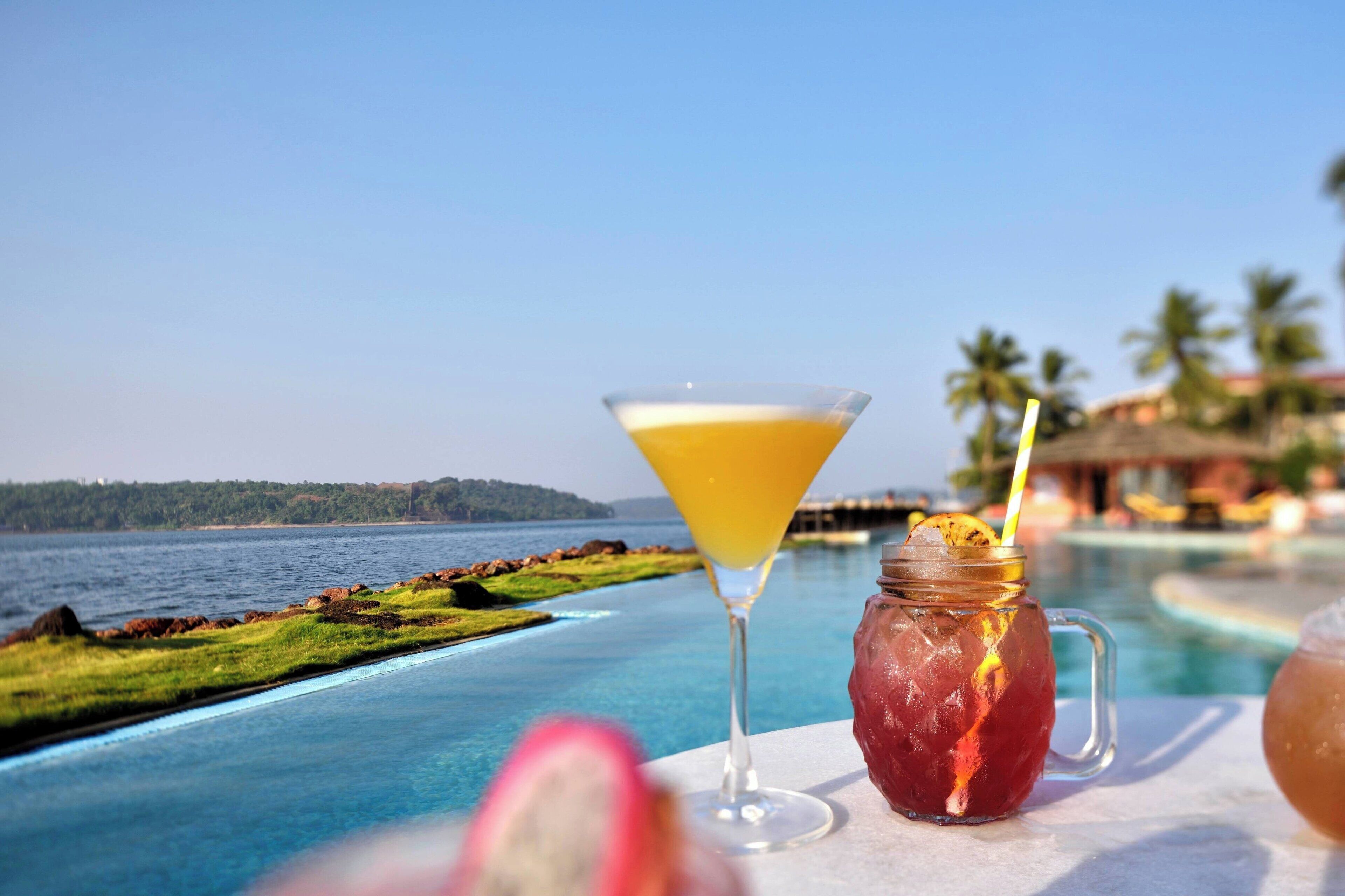 Une vue sur la piscine, avec une vue dégagée sur la mer, un verre à martini et une tasse contenant une boisson.