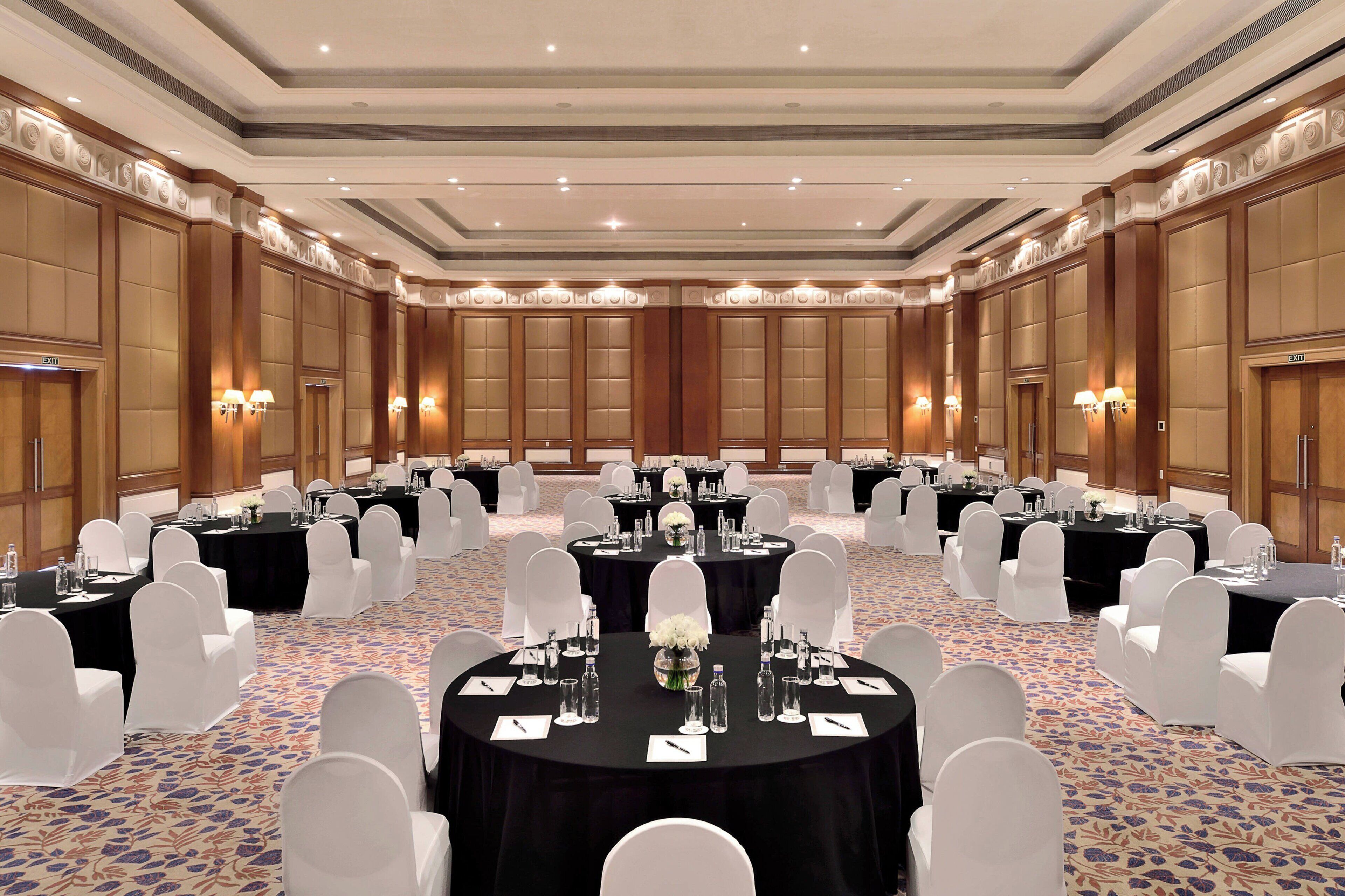 A large conference room with round tables, white chairs, and black tablecloths.
