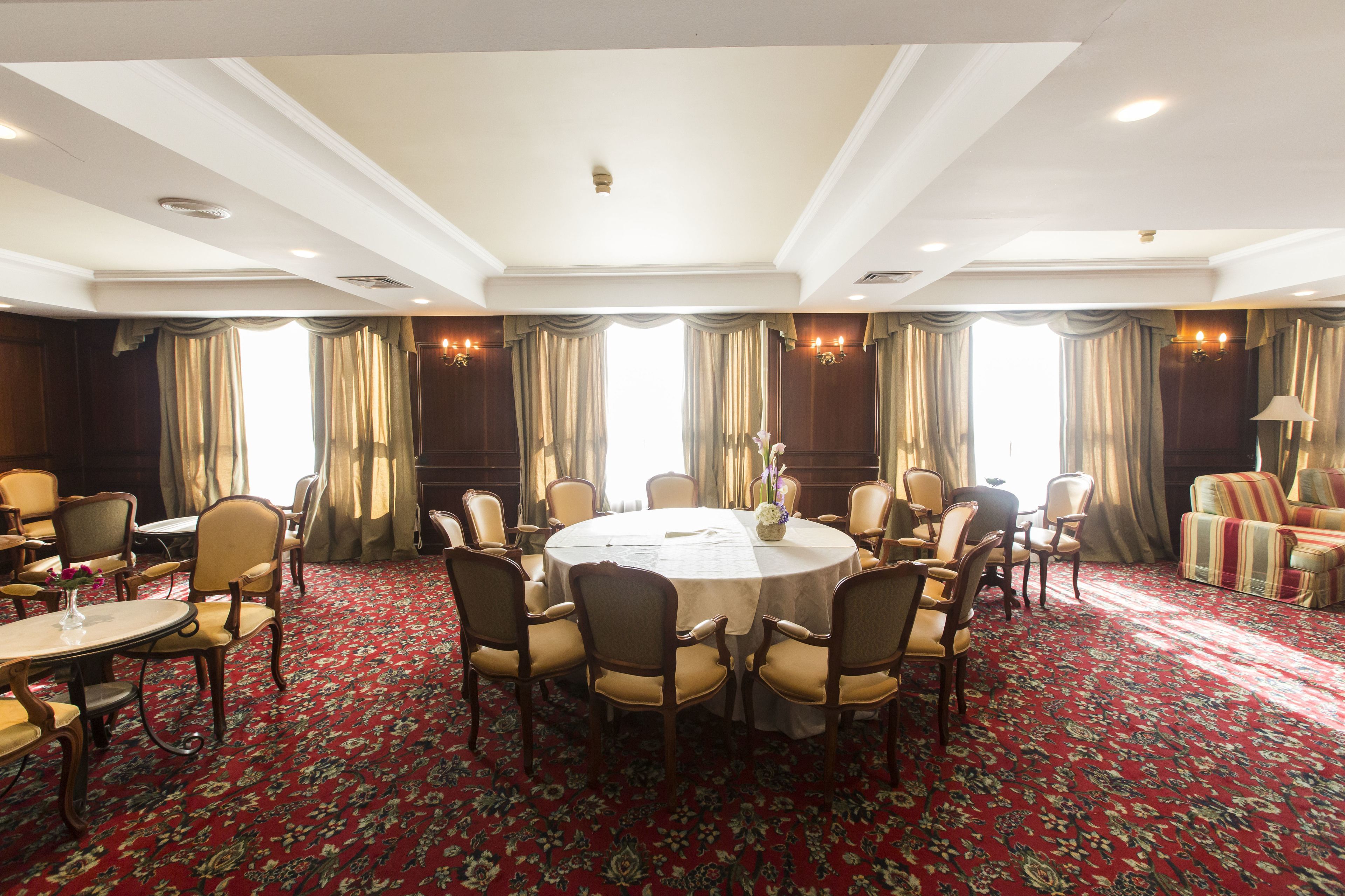 Quarto de hotel com uma mesa de jantar redonda rodeada por cadeiras, um sofá e um abajur.