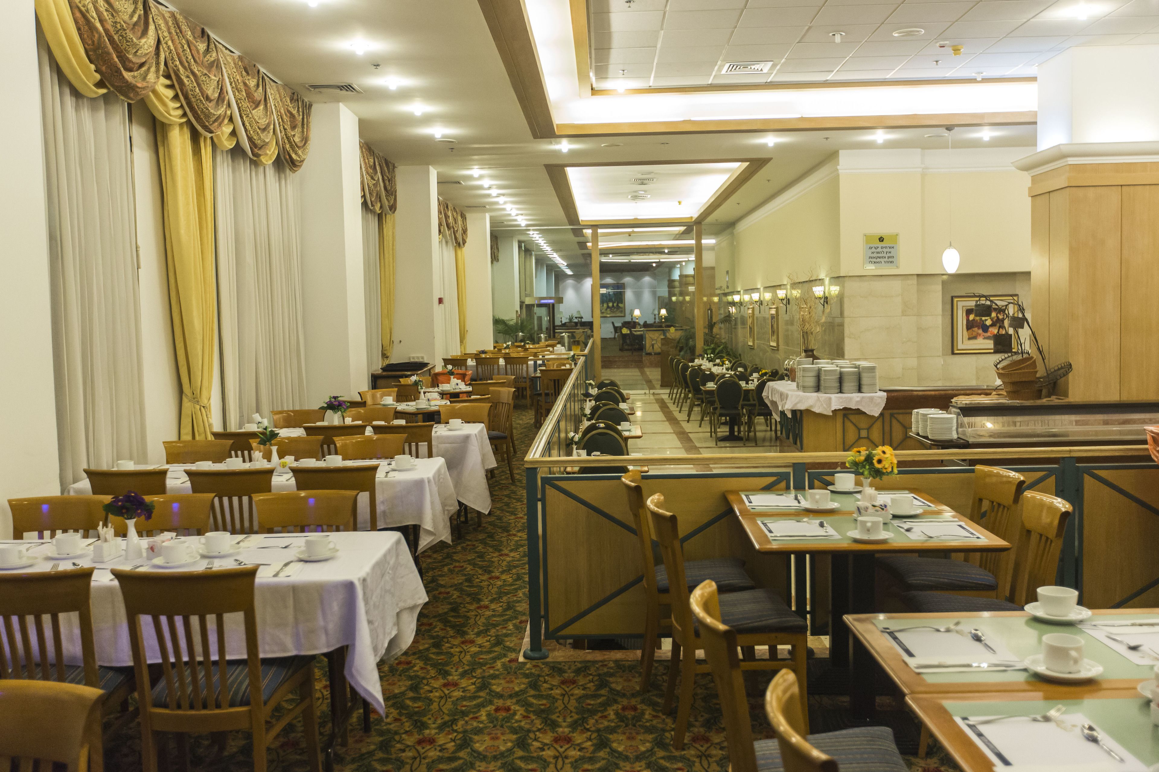Un comedor de hotel con varias mesas y sillas, una larga barra y vistas al pasillo.