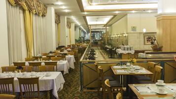 Un comedor de hotel con varias mesas y sillas, una larga barra y vistas al pasillo.