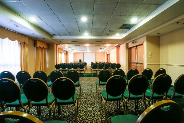 A conference room with rows of chairs, a projector screen, and a carpeted floor. - Nazareth Plaza Hotel (Nazareth Iliit)