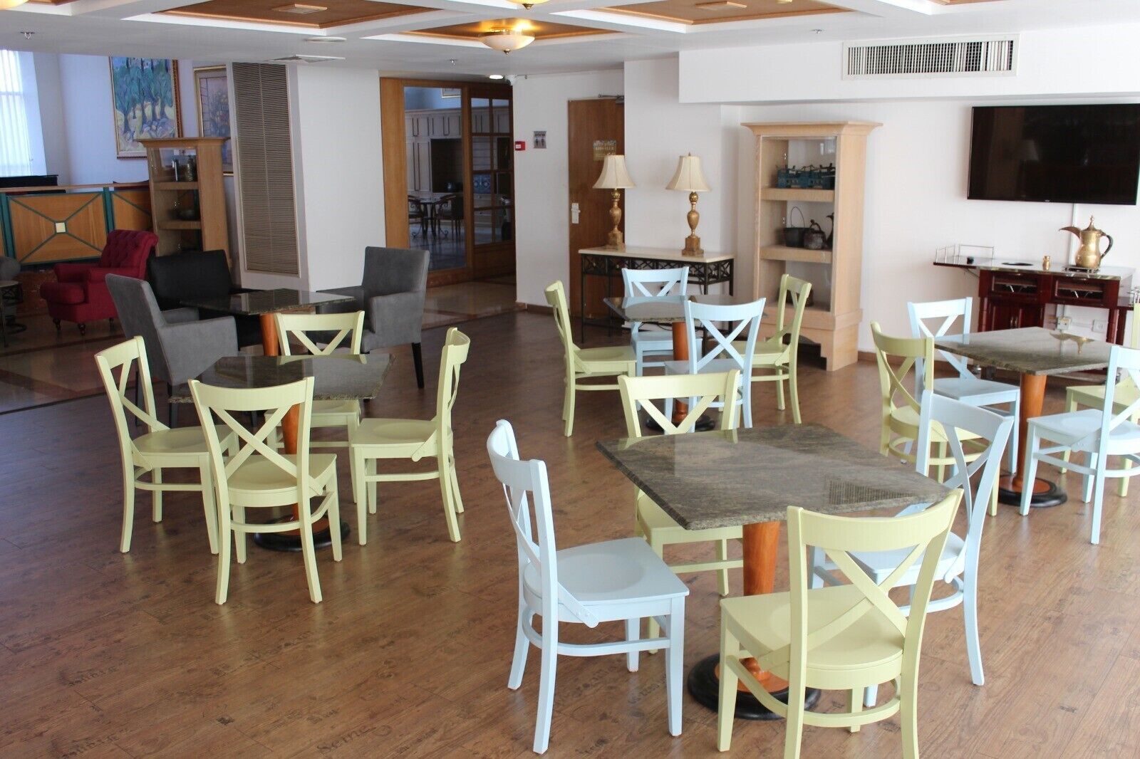 A spacious dining area with multiple tables and chairs, a television mounted on the wall, and a wooden ceiling with recessed lighting.