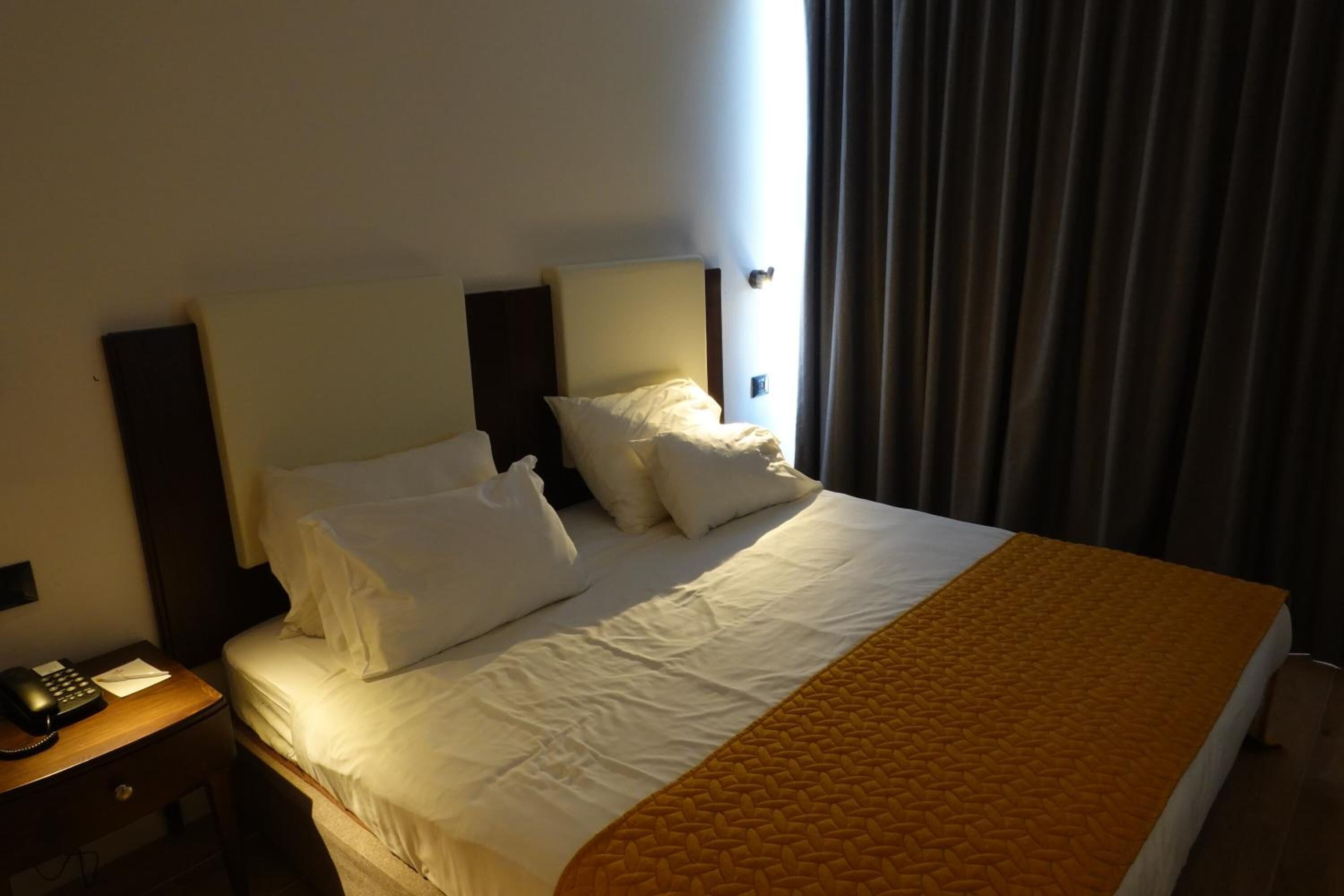 A hotel room with a large bed, a bedside table with a telephone, and a window with curtains.