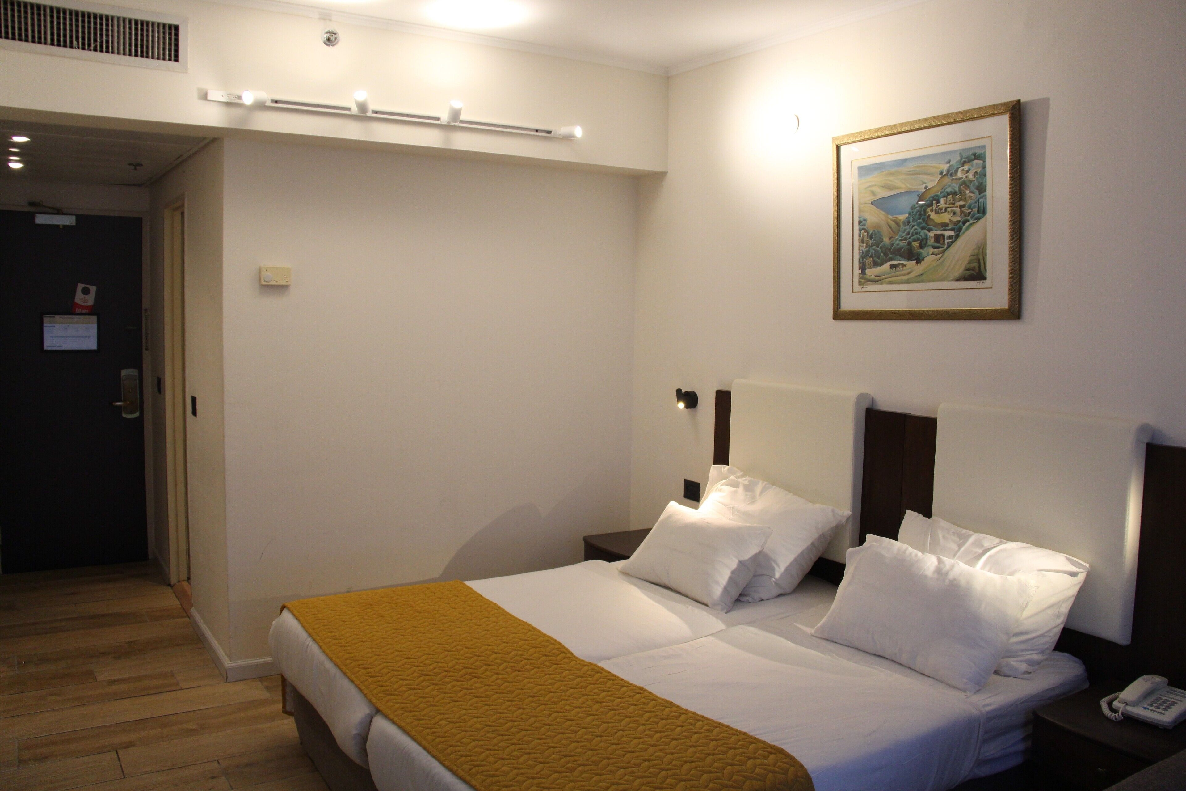 A hotel room with a bed, bedside tables, a telephone, and a painting on the wall.