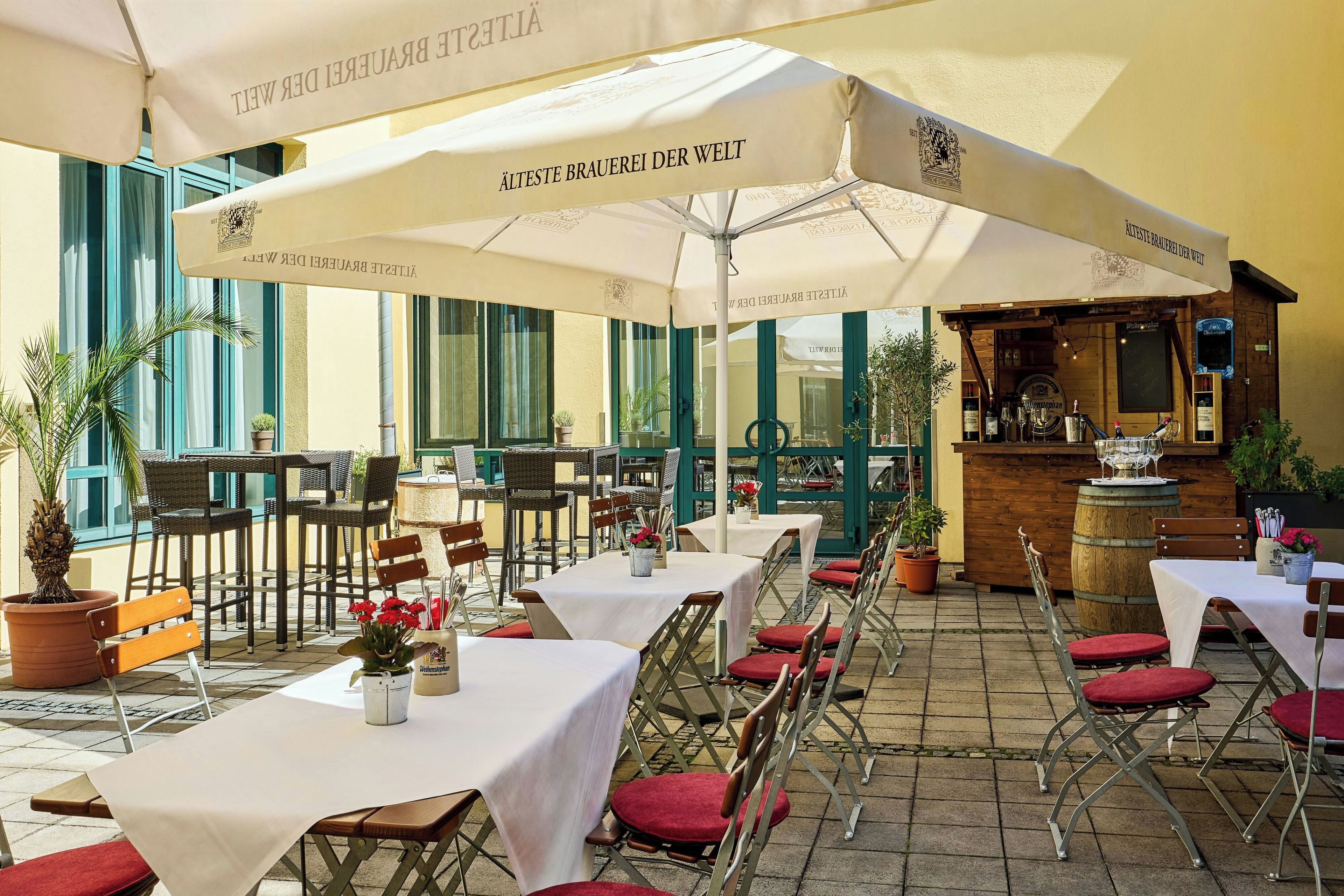 An outdoor dining area with tables and chairs, umbrellas, and a bar area.