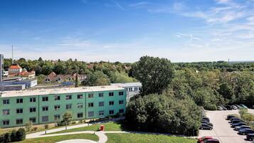 Un bâtiment vert doté de nombreuses fenêtres, un parking avec plusieurs voitures et un grand arbre au premier plan.
