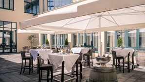 Un espace extérieur aménagé pour les repas, avec des tables et des chaises, protégé par de grands parasols, et agrémenté d’une fontaine décorative.
