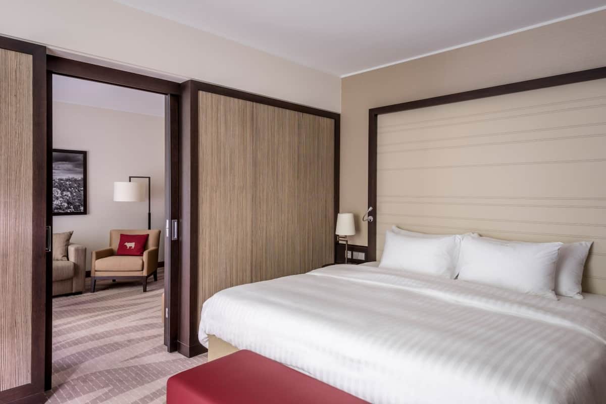 A hotel room with a large bed, a red bench, a chair, a desk, and a lamp.