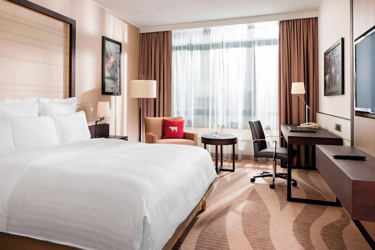 A hotel room with a large bed, a desk, a chair, a small table, and a TV.