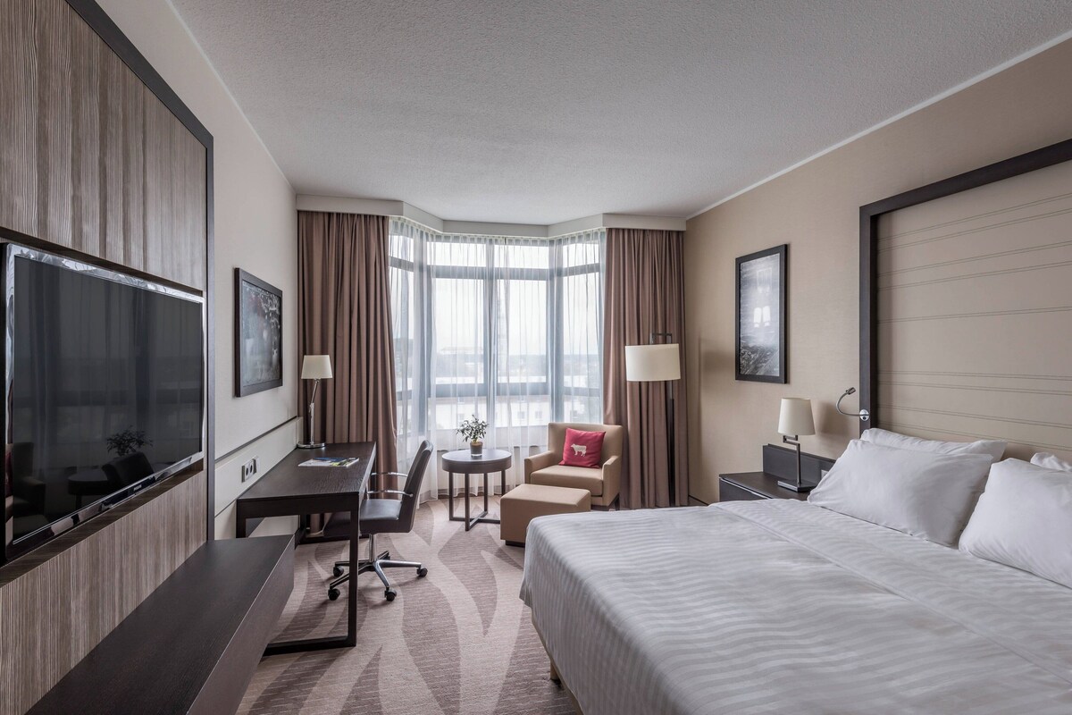 Une chambre d’hôtel avec un grand lit, un bureau, une chaise, une petite table et un téléviseur.