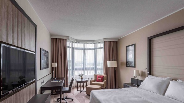Habitación de hotel con una cama grande, un escritorio, una silla, una mesita con una planta y un televisor.