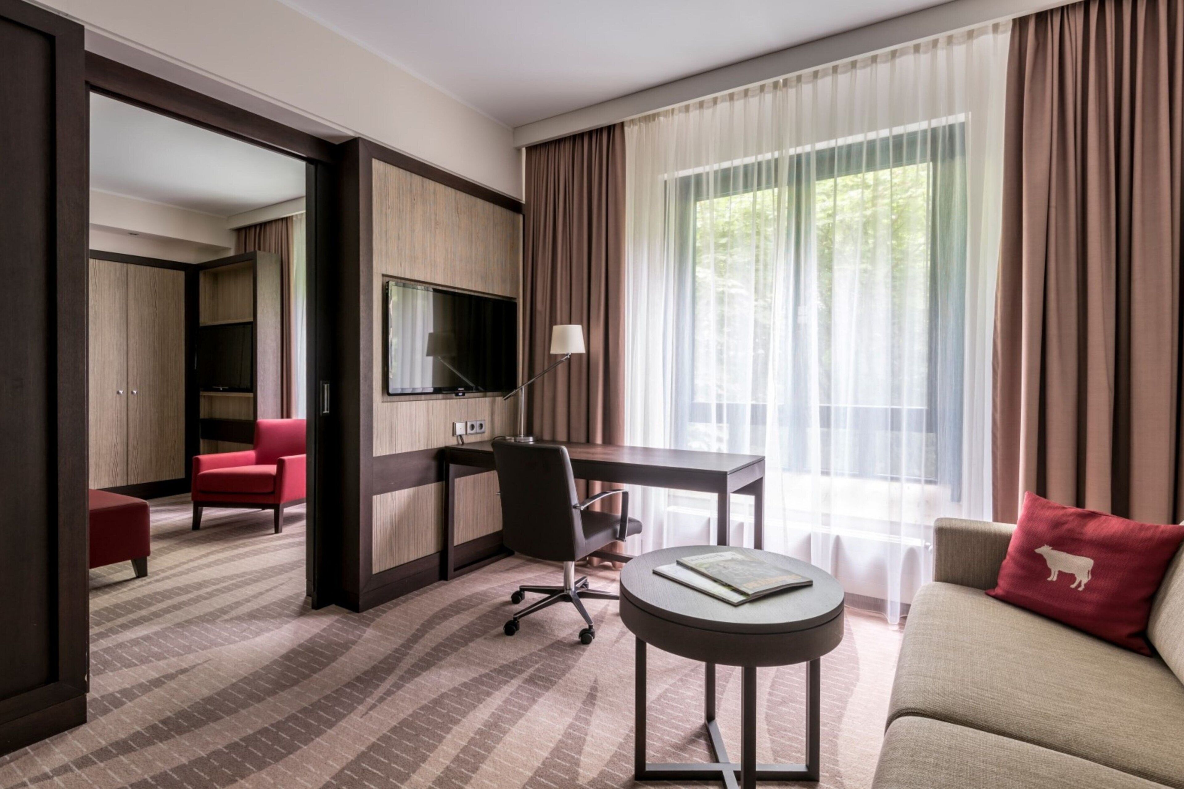 A hotel room with a desk, chair, sofa, and a TV.