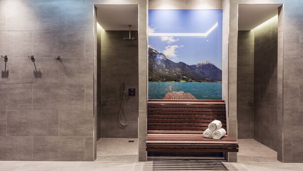 Une salle de bain moderne avec un banc, une douche et une grande fresque représentant un lac et des montagnes.