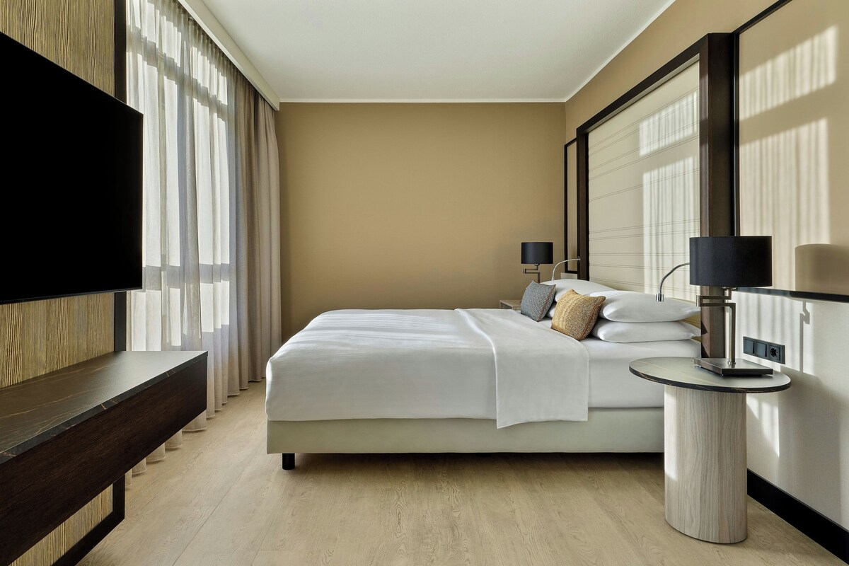 A hotel room with a bed, bedside lamps, a TV, and a round table.