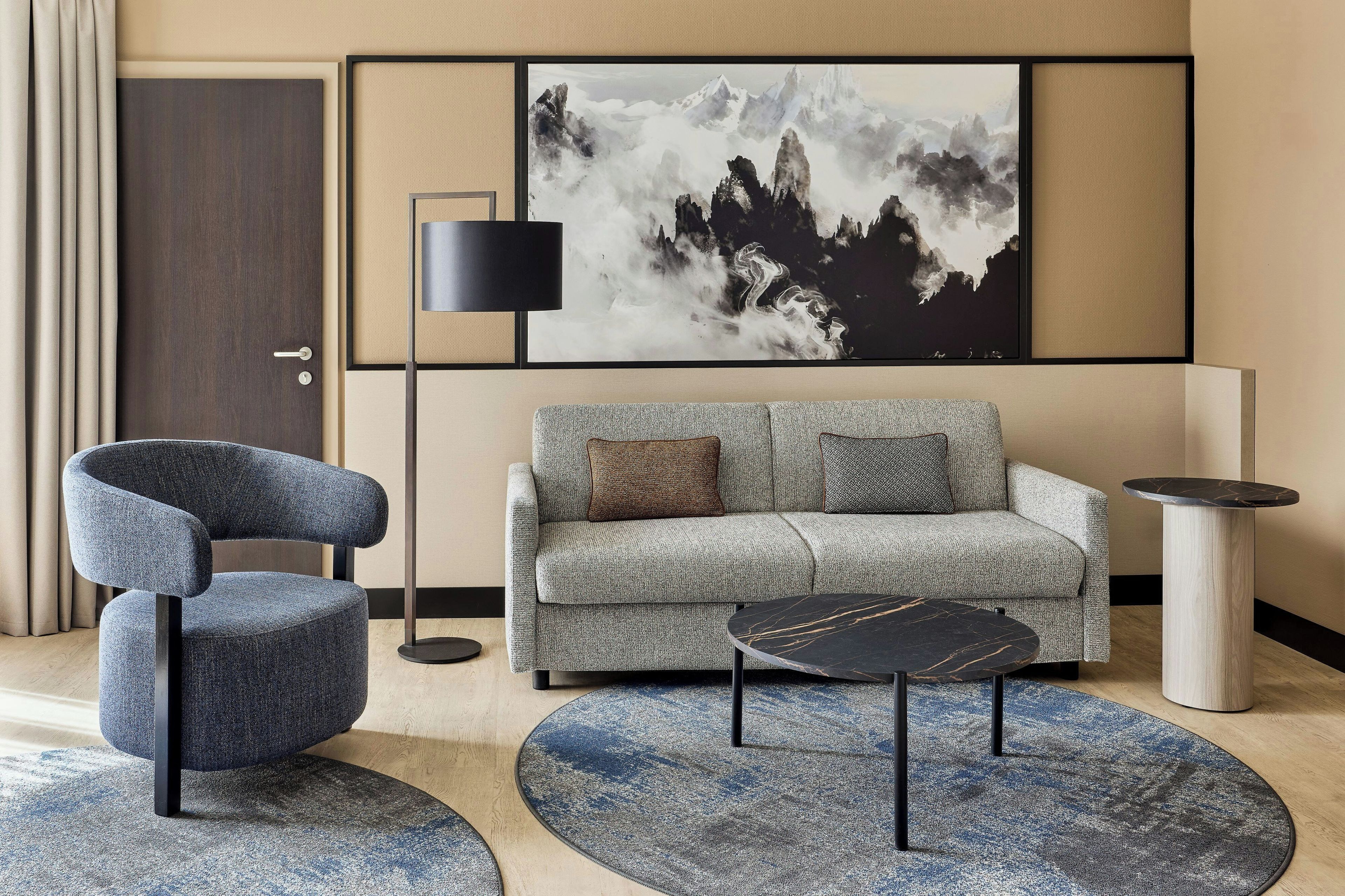 A modern living room with a sofa, a chair, a coffee table, and a large painting on the wall.