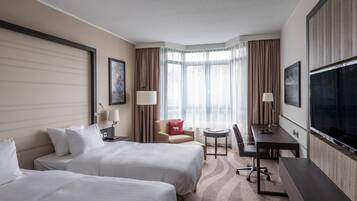 Habitación de hotel con dos camas, un escritorio, una silla, un televisor y una ventana con cortinas.