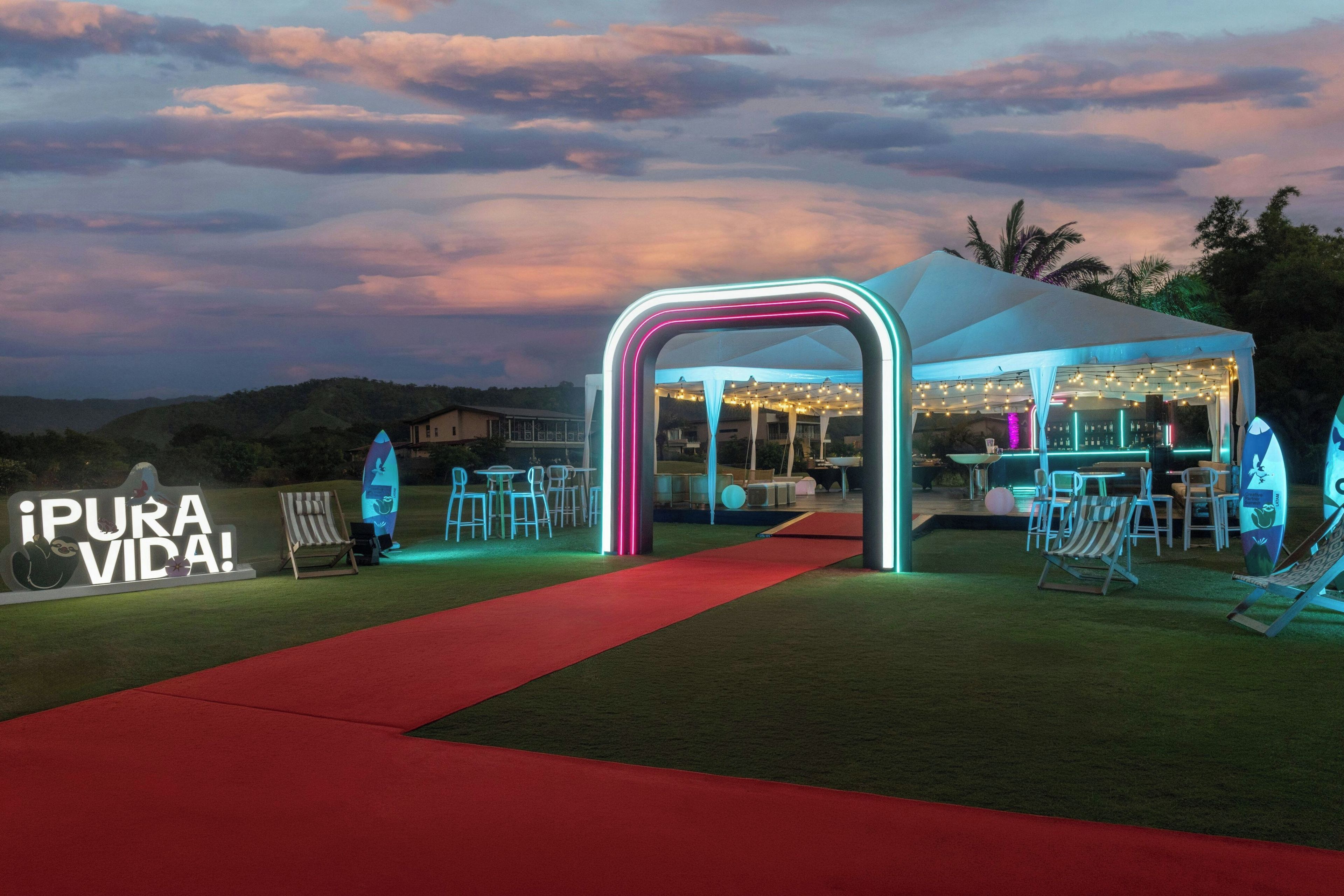 An outdoor event space with a red carpet leading to a tented area with tables and chairs.