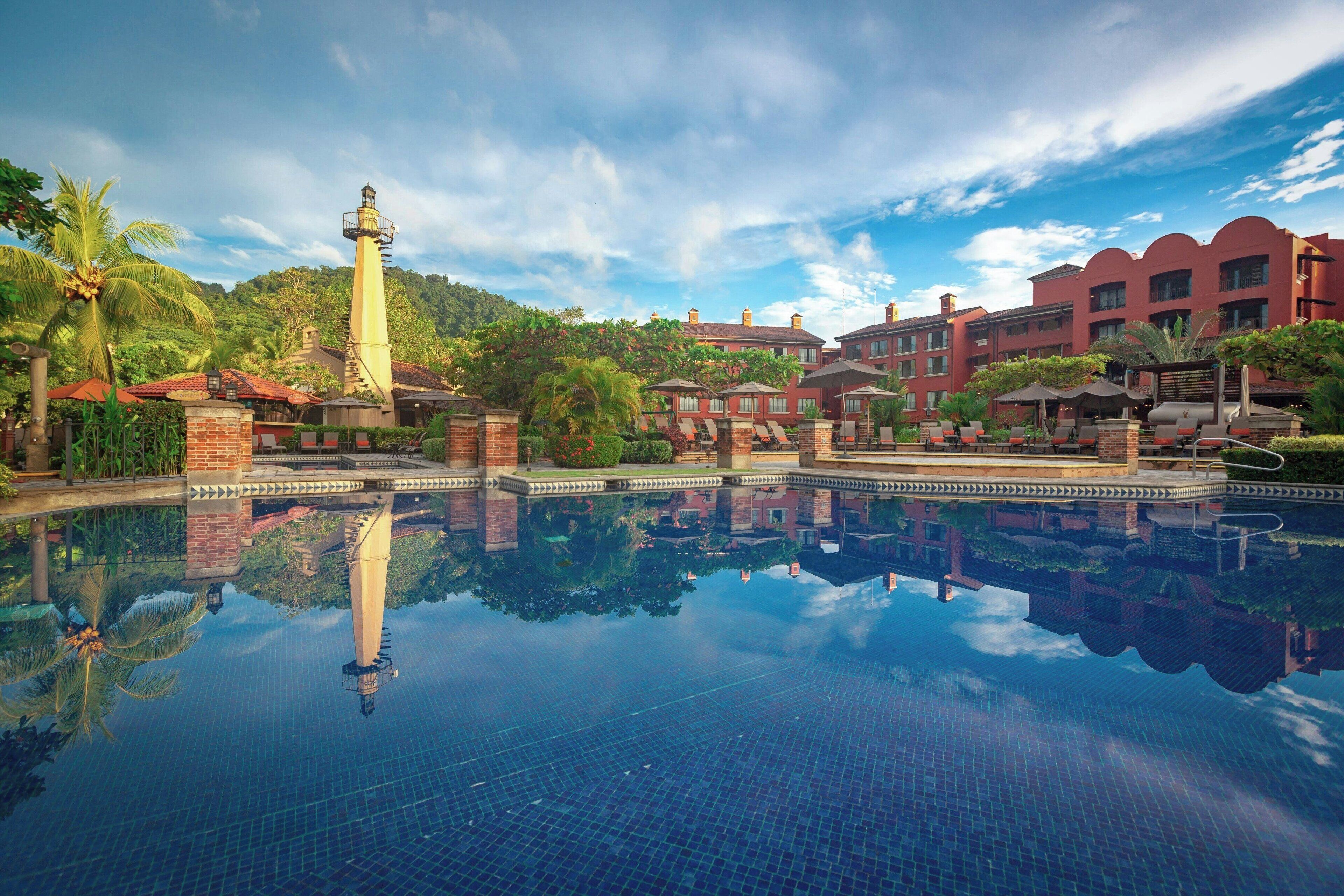A hotel with a large pool reflecting the surrounding buildings and a lighthouse.