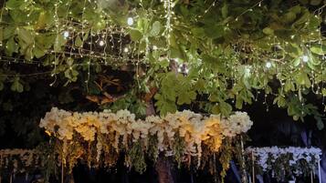 An outdoor wedding setup with a canopy of white flowers, string lights, and a table with candles.