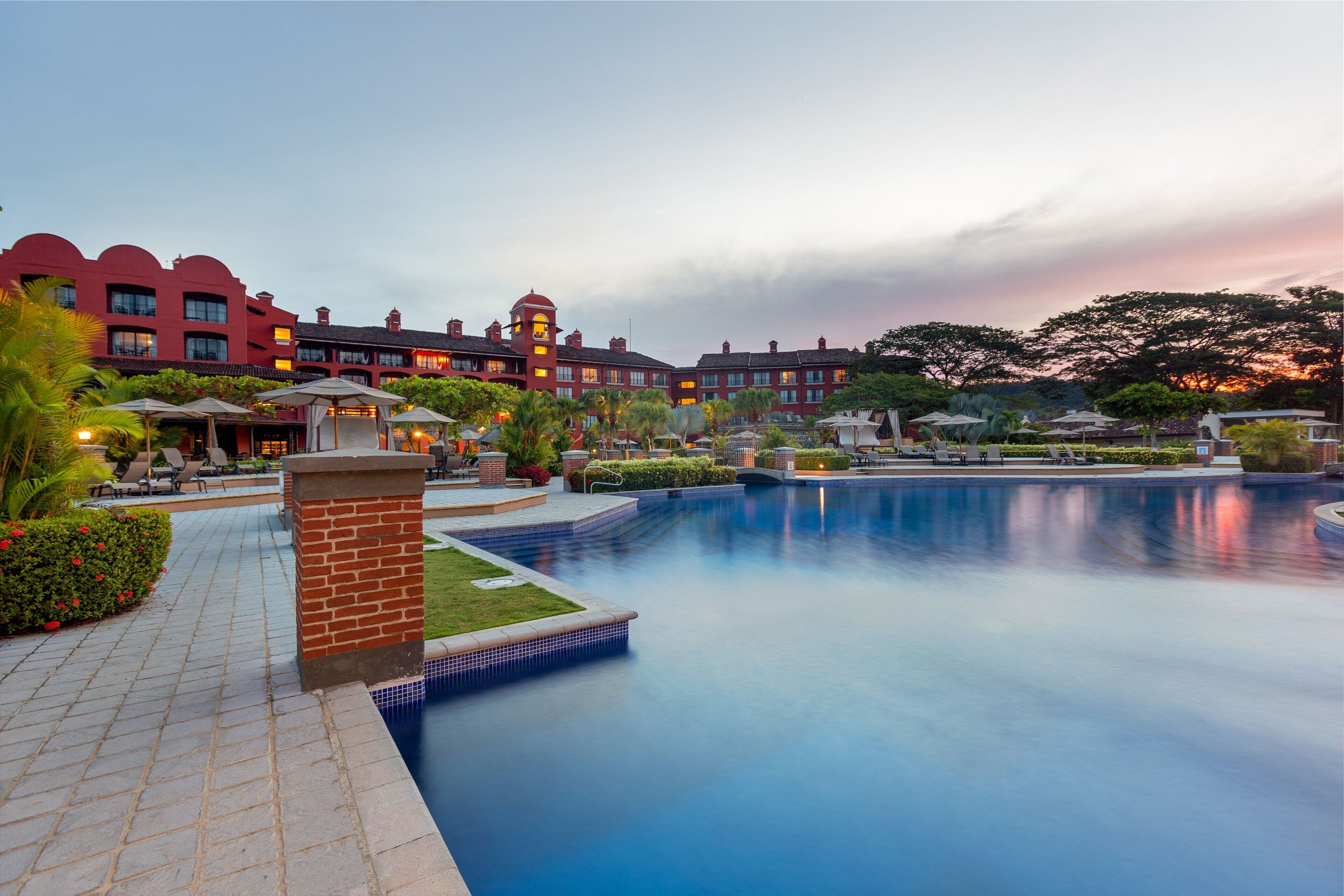 Ein Hotel mit großem Pool, Sitzgelegenheiten im Freien und einem gepflegten Garten.