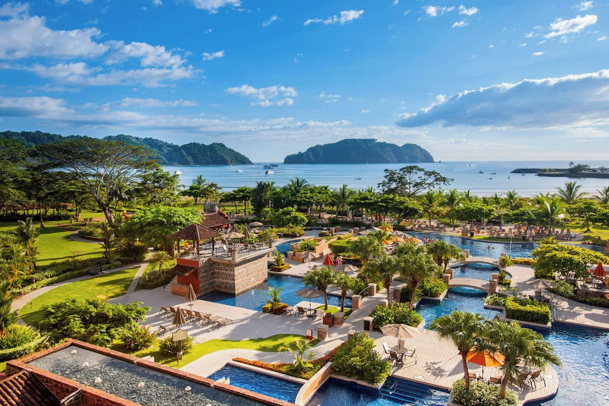 A resort with multiple swimming pools, lush greenery, and a view of the sea.