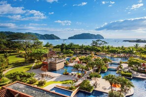 Un resort con varias piscinas, abundante vegetación y vista al mar.
