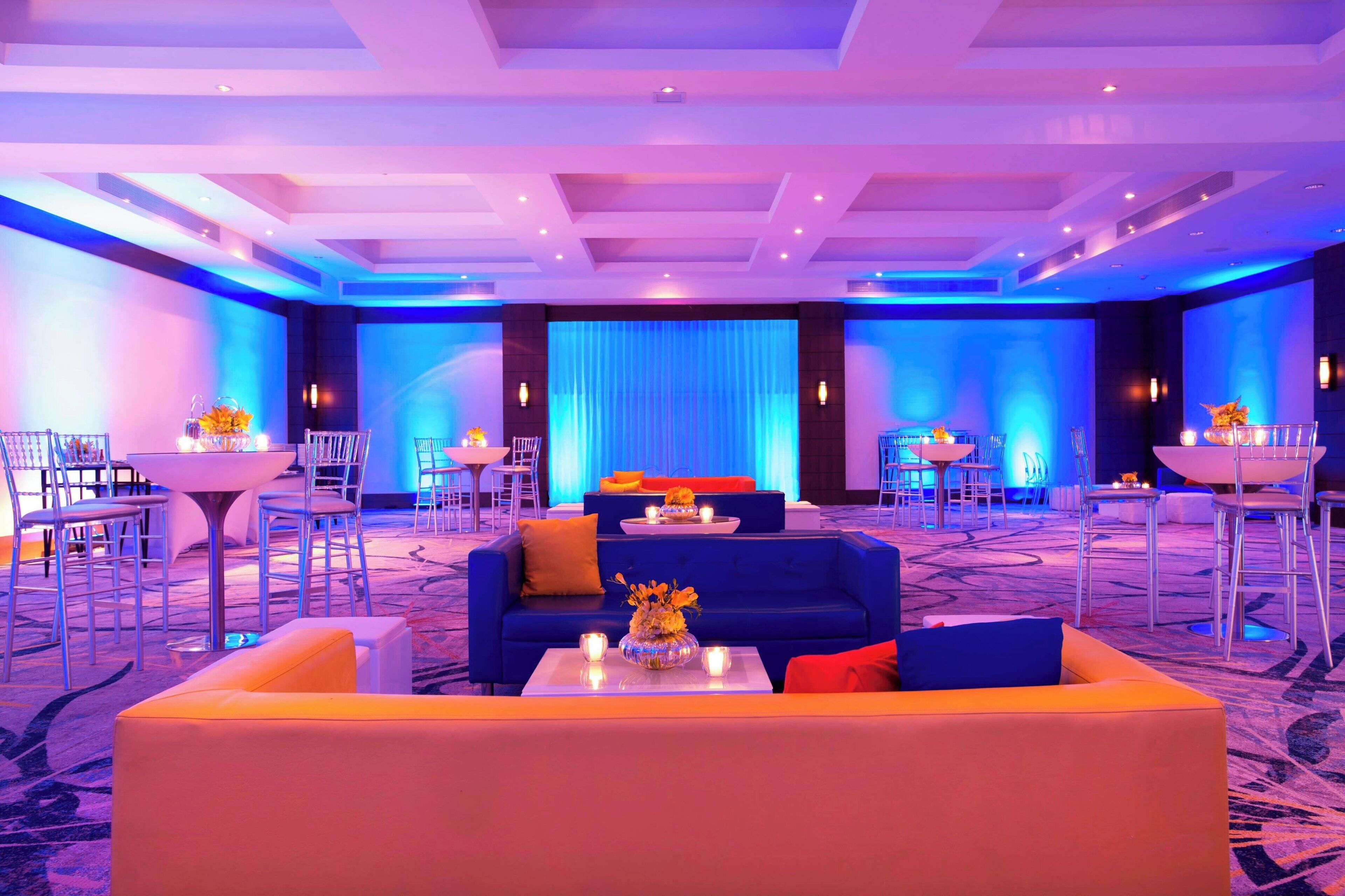 Un vestíbulo de hotel con un escenario iluminado en azul, zonas de estar y piso alfombrado.