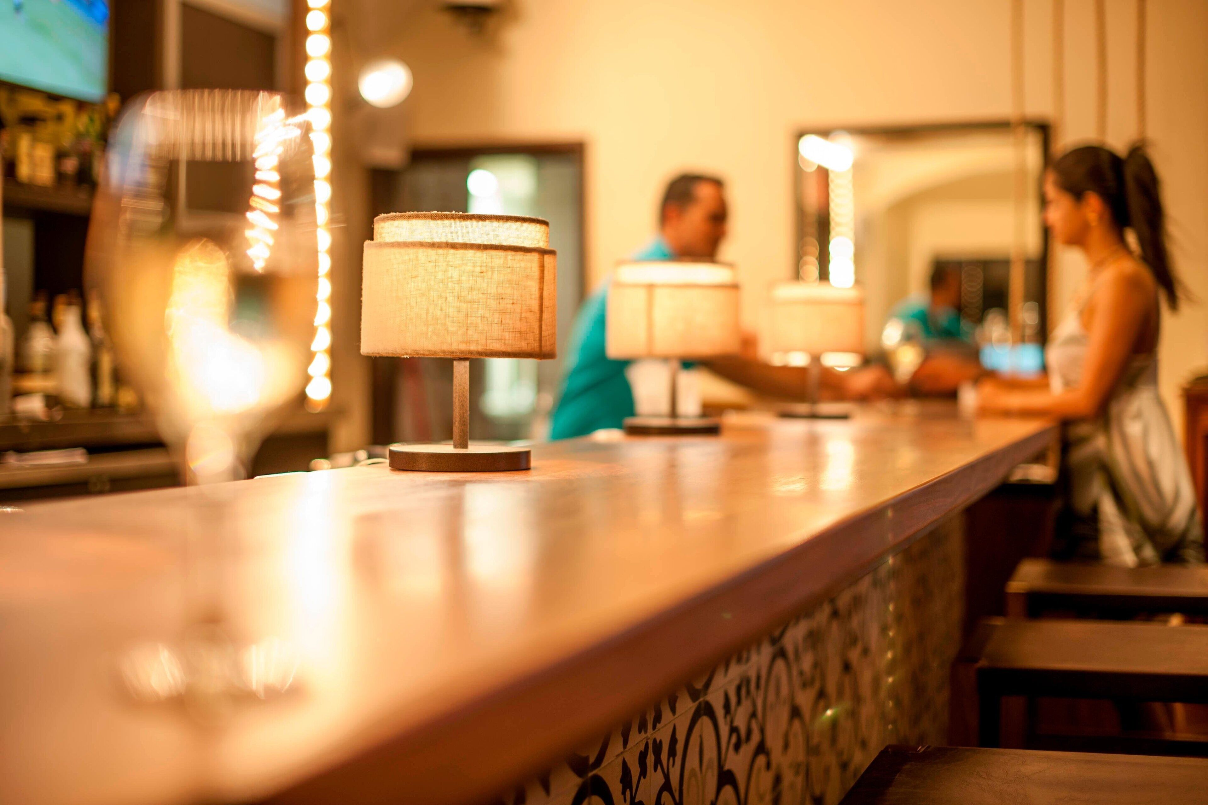 A bar area with a counter, lamps, and a person in the background.