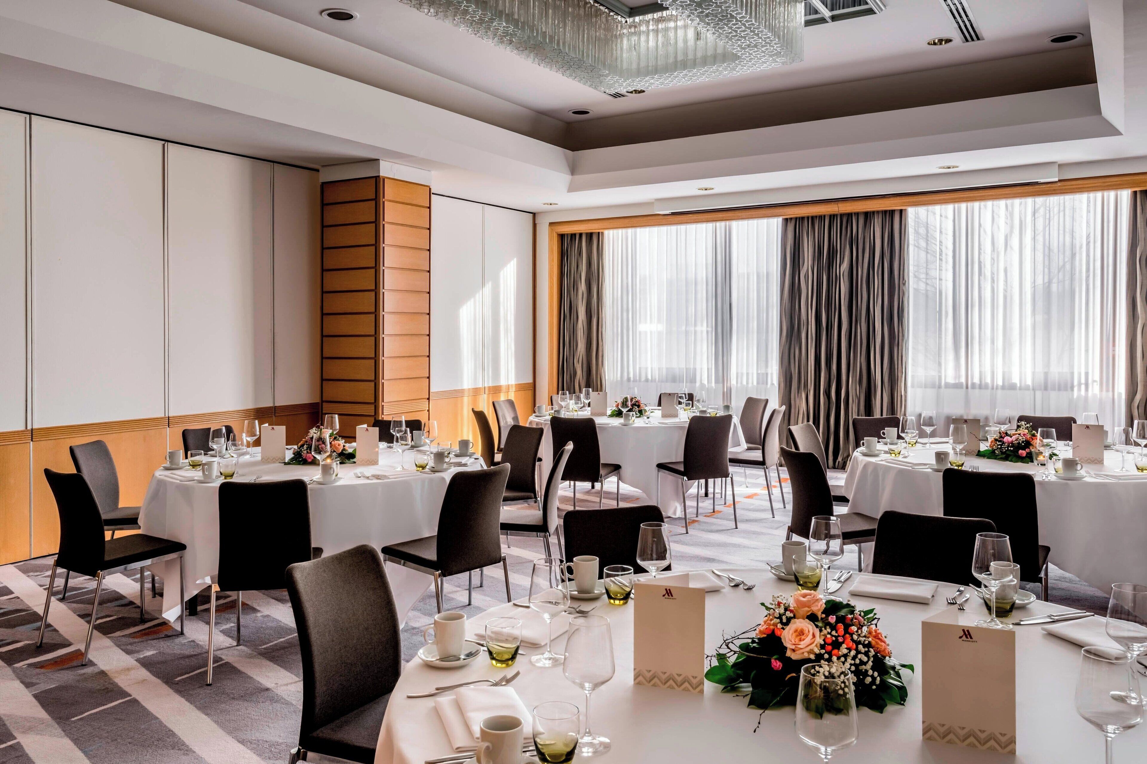 A banquet hall with round tables set for dining, equipped with chairs, table settings, and floral centerpieces.