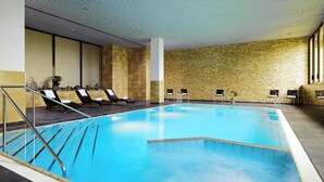 An indoor swimming pool with lounge chairs and a stone wall. - Stuttgart Marriott Hotel Sindelfingen (Sindelfingen)