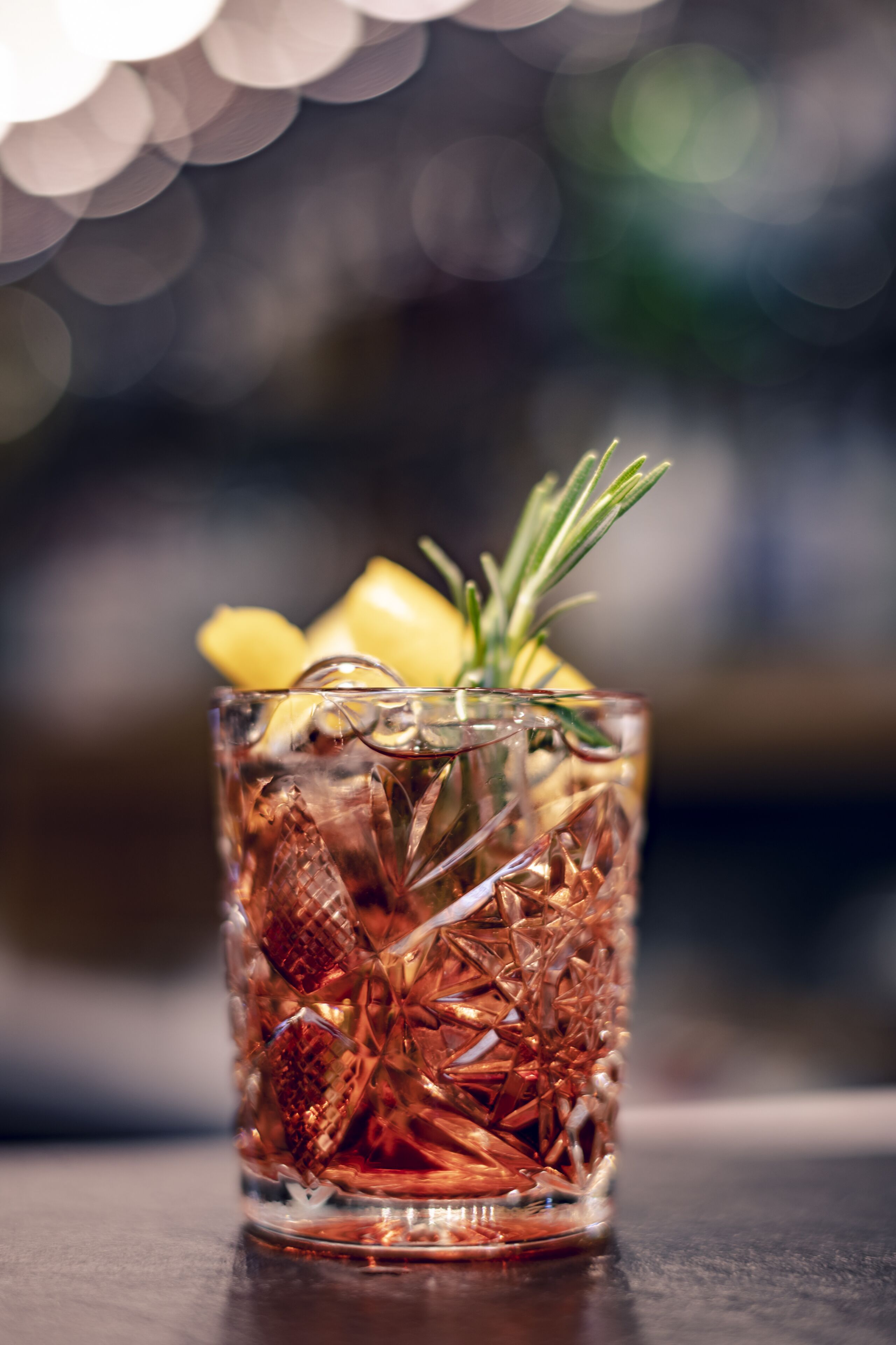 A clear glass with ice cubes and a sprig of rosemary on top.