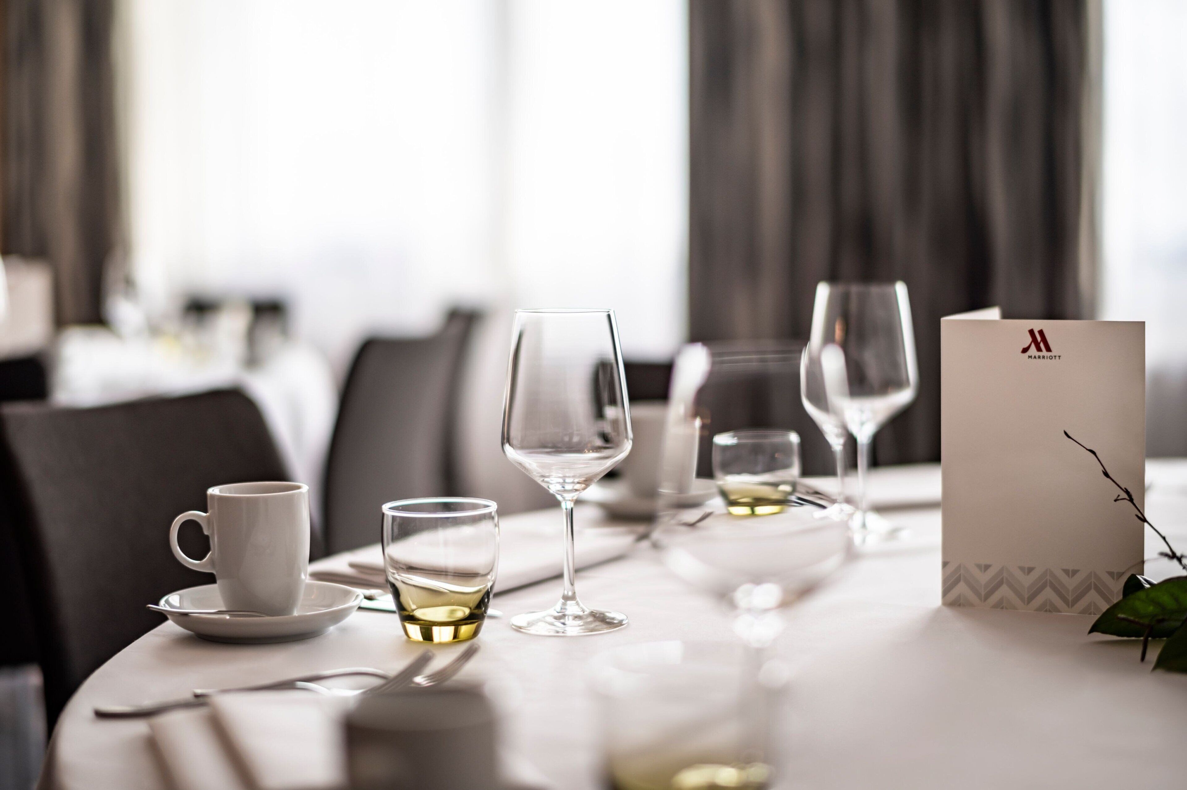 A dining table set with a white cup, two wine glasses, and a menu card in a hotel setting.
