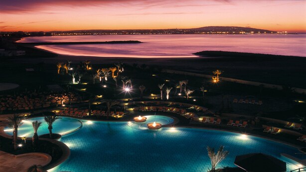 A large outdoor swimming pool with multiple seating areas and a view of the ocean at dusk. - Mövenpick Hotel & Casino Malabata Tanger (Tangier)