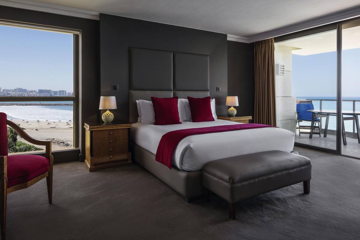 A hotel room with a large bed, a chair, a table, and a view of the beach.