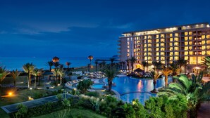 A hotel with a pool, palm trees, and a view of the ocean. - Mövenpick Hotel & Casino Malabata Tanger (Tangier)
