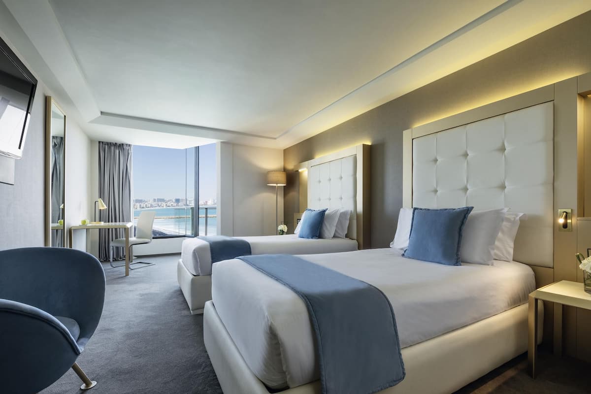 A hotel room with a large bed, a desk, a chair, and a view of the city.