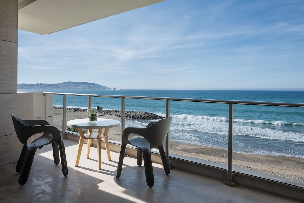 A balcony with a view of the ocean, two chairs, and a small table.