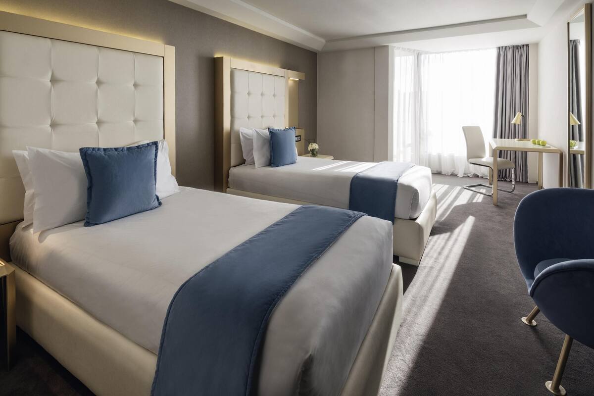 A hotel room with two beds, a desk, and a chair.