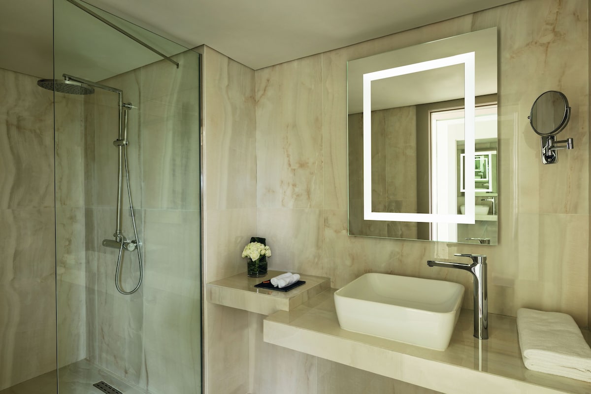 A modern bathroom with a glass-enclosed shower, a white sink, and a mirror with a round frame.